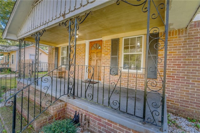 doorway to property with a porch, fence, and brick siding