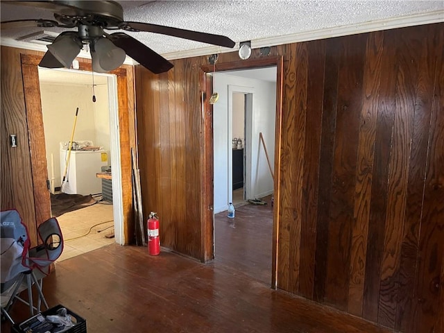 corridor with washer and dryer, a textured ceiling, ornamental molding, dark hardwood / wood-style floors, and wooden walls