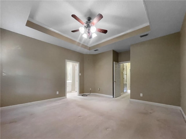 spare room with a raised ceiling, ceiling fan, crown molding, and light colored carpet