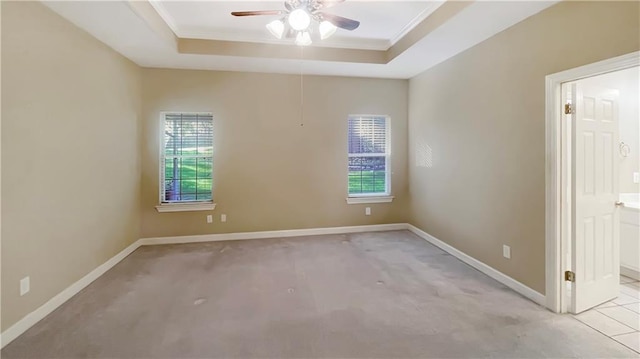 empty room featuring ceiling fan, a raised ceiling, light carpet, and crown molding