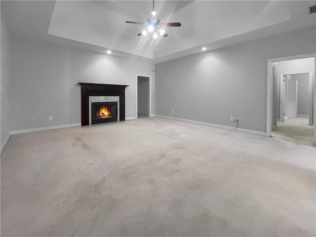 unfurnished living room with a raised ceiling, a premium fireplace, ceiling fan, and light colored carpet