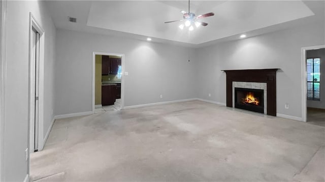 unfurnished living room with a raised ceiling, ceiling fan, a high end fireplace, and light colored carpet