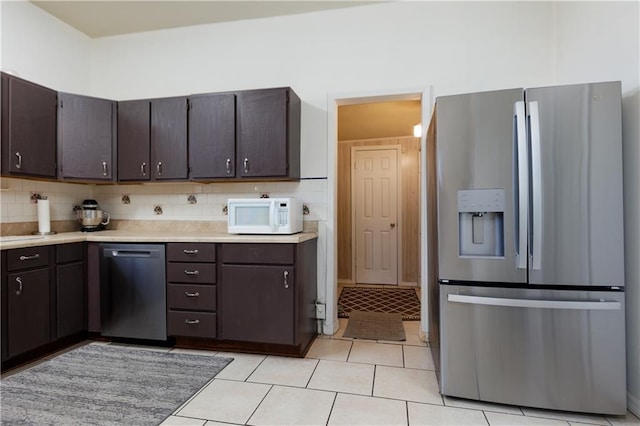 kitchen with stainless steel appliances, dark brown cabinetry, light countertops, light tile patterned floors, and decorative backsplash