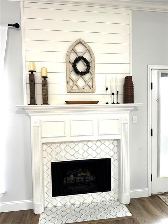 room details featuring a tiled fireplace, wood finished floors, and baseboards