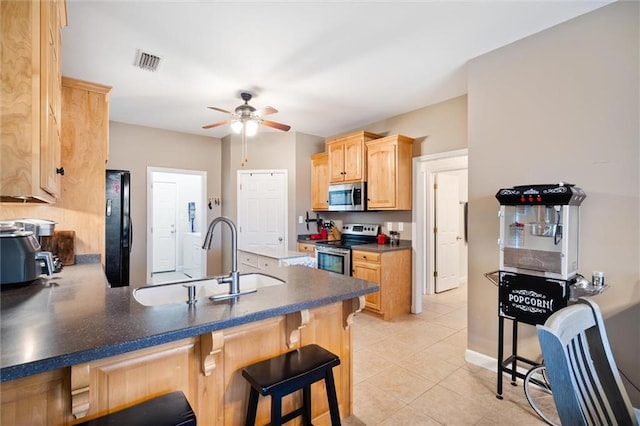 kitchen featuring appliances with stainless steel finishes, a kitchen bar, light tile floors, light brown cabinetry, and ceiling fan