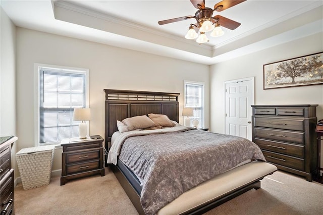 bedroom with ceiling fan, crown molding, a tray ceiling, and light colored carpet