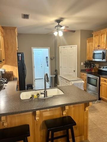 kitchen with appliances with stainless steel finishes, sink, ceiling fan, light tile flooring, and a kitchen bar