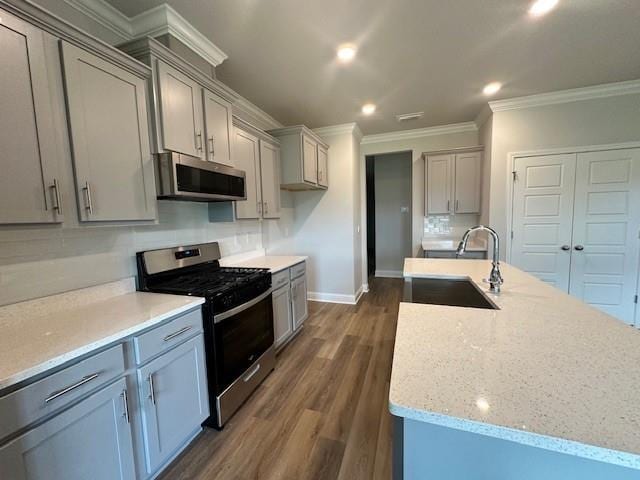 kitchen featuring dark hardwood / wood-style flooring, a kitchen island with sink, stainless steel appliances, ornamental molding, and sink