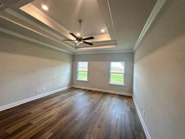 empty room with dark wood-type flooring, ceiling fan, ornamental molding, and a tray ceiling