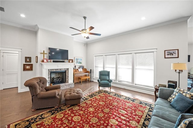 living room with a fireplace with raised hearth, wood finished floors, a ceiling fan, and crown molding