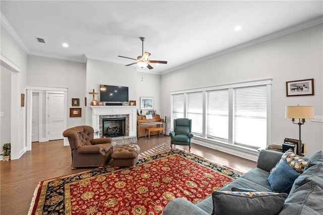 living area with a fireplace with raised hearth, ornamental molding, wood finished floors, and visible vents