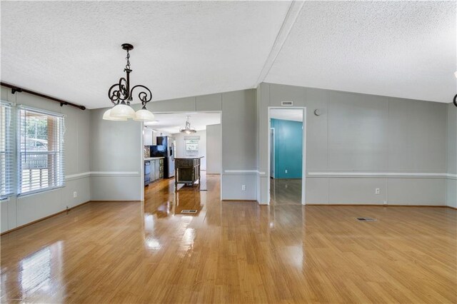 3628 Jarvis Ln, Semmes, AL 36575 - unfurnished living room with a textured ceiling, light wood finished floors, a chandelier, baseboards, and lofted ceiling