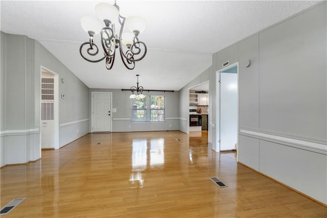 3628 Jarvis Ln, Semmes, AL 36575 - unfurnished dining area with a chandelier, light wood-style floors, vaulted ceiling, a textured ceiling, and a decorative wall