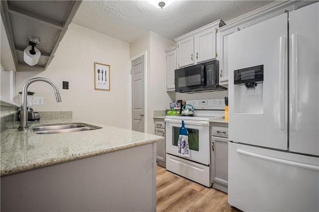 kitchen featuring white appliances, a sink, light wood-type flooring, a textured ceiling, and light stone countertops