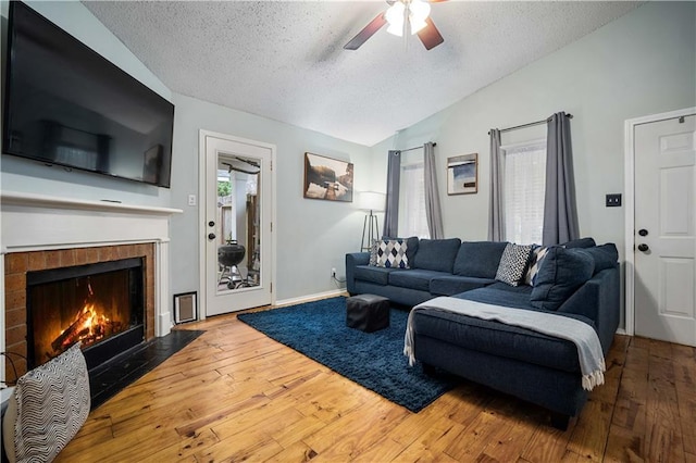 living area featuring a textured ceiling, vaulted ceiling, ceiling fan, hardwood / wood-style floors, and a tile fireplace