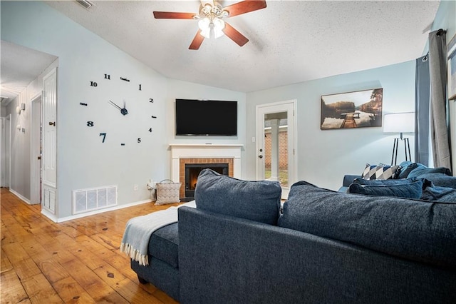 living room featuring a textured ceiling, vaulted ceiling, a ceiling fan, wood-type flooring, and a fireplace