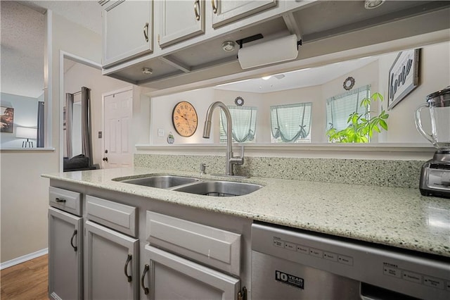 kitchen featuring stainless steel dishwasher, a sink, wood finished floors, and light stone counters
