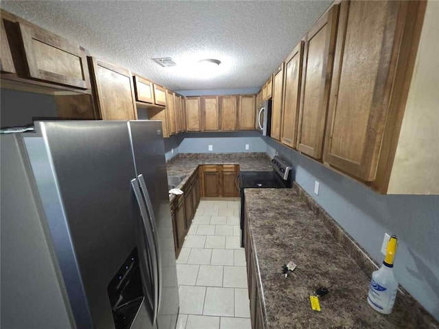 1105 Adams St, Mobile, AL 36603 - kitchen featuring appliances with stainless steel finishes, brown cabinets, a textured ceiling, dark stone countertops, and light tile patterned floors