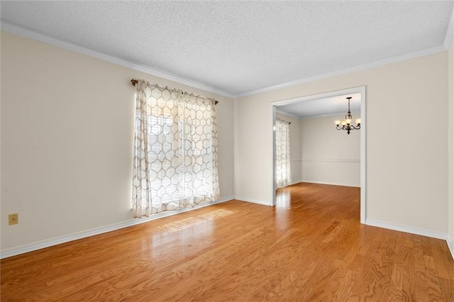 empty room featuring a textured ceiling, light hardwood / wood-style flooring, a notable chandelier, and crown molding