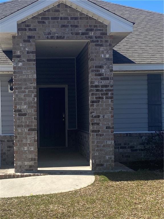 entrance to property featuring brick siding and a shingled roof