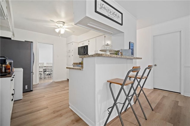 5554 Racine Ave, Mobile, AL 36618 - kitchen with black microwave, ceiling fan, light wood finished floors, white cabinetry, and a kitchen bar