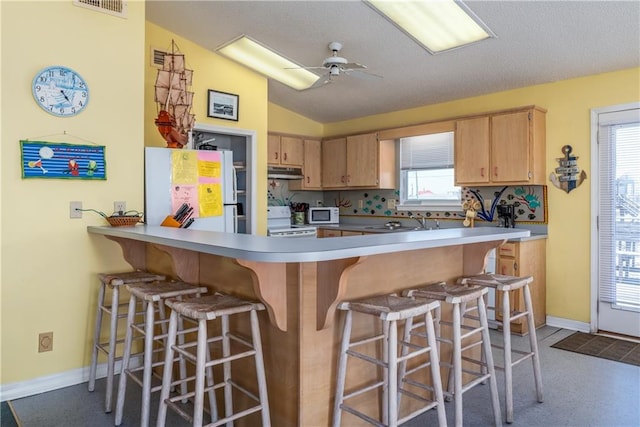 kitchen with white appliances, baseboards, a peninsula, lofted ceiling, and under cabinet range hood