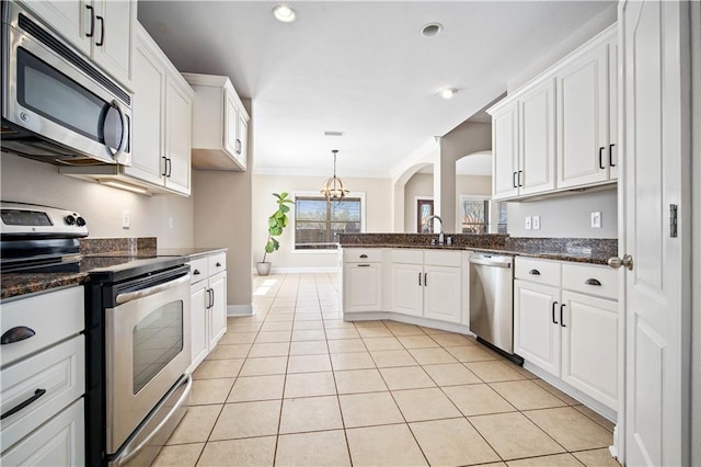 kitchen featuring a sink, white cabinetry, stainless steel appliances, arched walkways, and light tile patterned floors