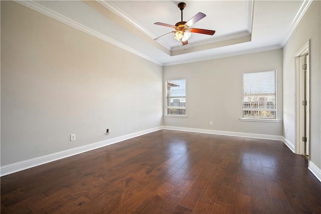 unfurnished room featuring a tray ceiling, dark wood-type flooring, a wealth of natural light, and ornamental molding