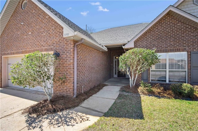 doorway to property featuring brick siding, concrete driveway, an attached garage, and a shingled roof