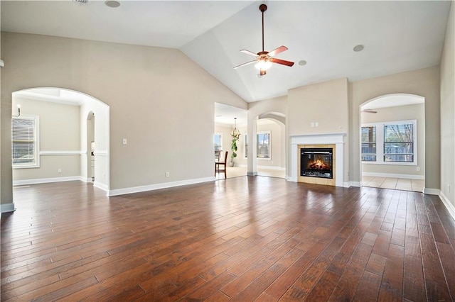 unfurnished living room with a ceiling fan, baseboards, dark wood finished floors, arched walkways, and a glass covered fireplace