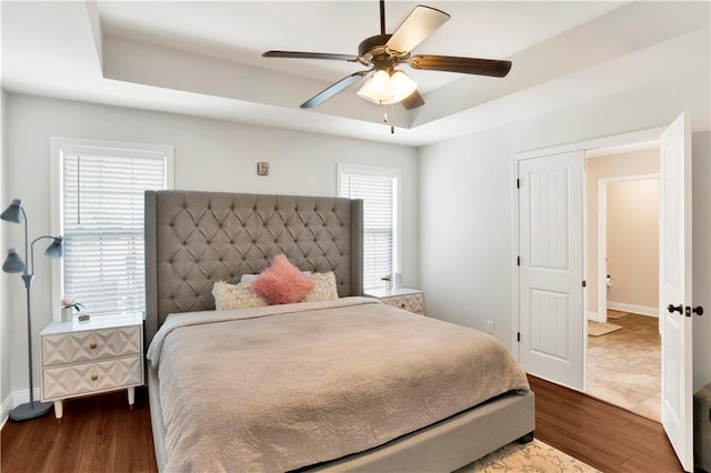 bedroom featuring baseboards, a raised ceiling, wood finished floors, and a ceiling fan