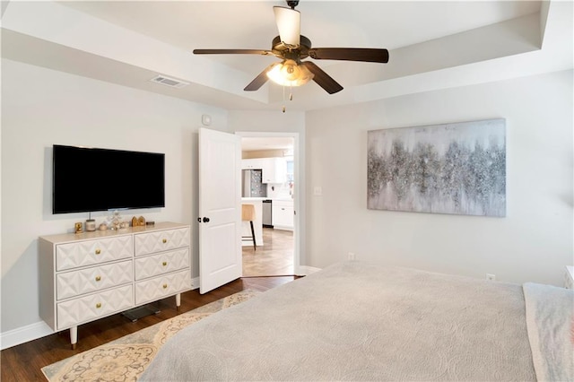 bedroom featuring visible vents, dark wood-type flooring, a tray ceiling, baseboards, and ceiling fan