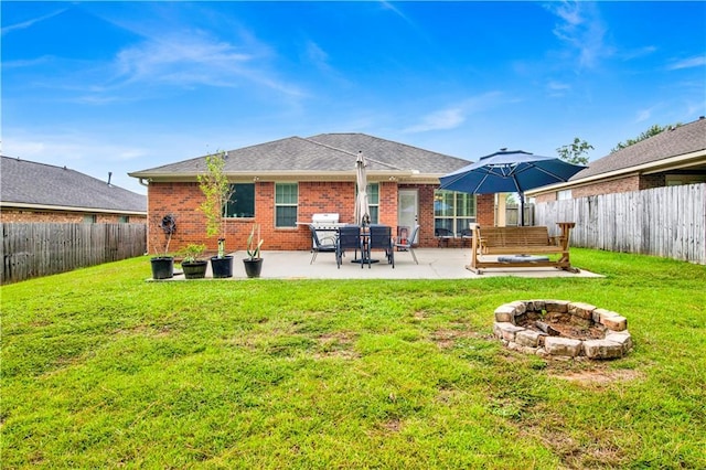 back of property featuring a yard, a fenced backyard, brick siding, and a fire pit