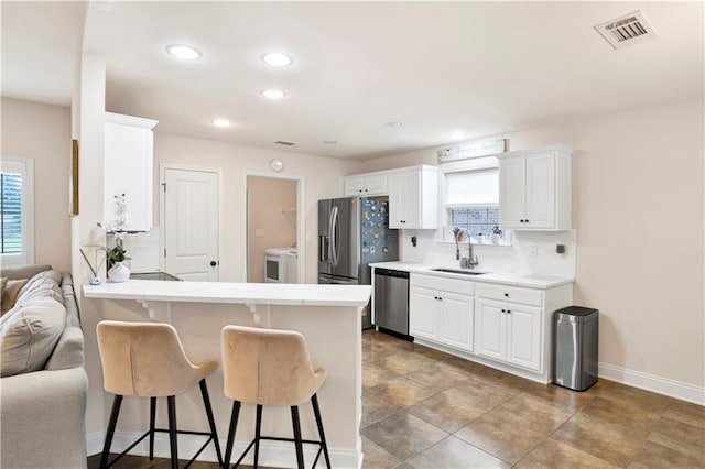 kitchen with visible vents, a kitchen bar, a sink, backsplash, and appliances with stainless steel finishes