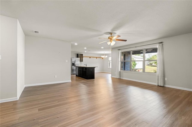 unfurnished living room with baseboards, visible vents, light wood-style flooring, a textured ceiling, and ceiling fan with notable chandelier