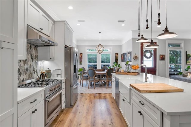 kitchen with appliances with stainless steel finishes, decorative light fixtures, sink, decorative backsplash, and a center island with sink