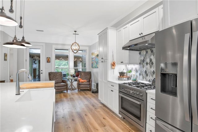 kitchen with white cabinets, decorative backsplash, hanging light fixtures, stainless steel appliances, and light hardwood / wood-style flooring