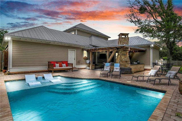 pool at dusk featuring an outdoor bar and a patio