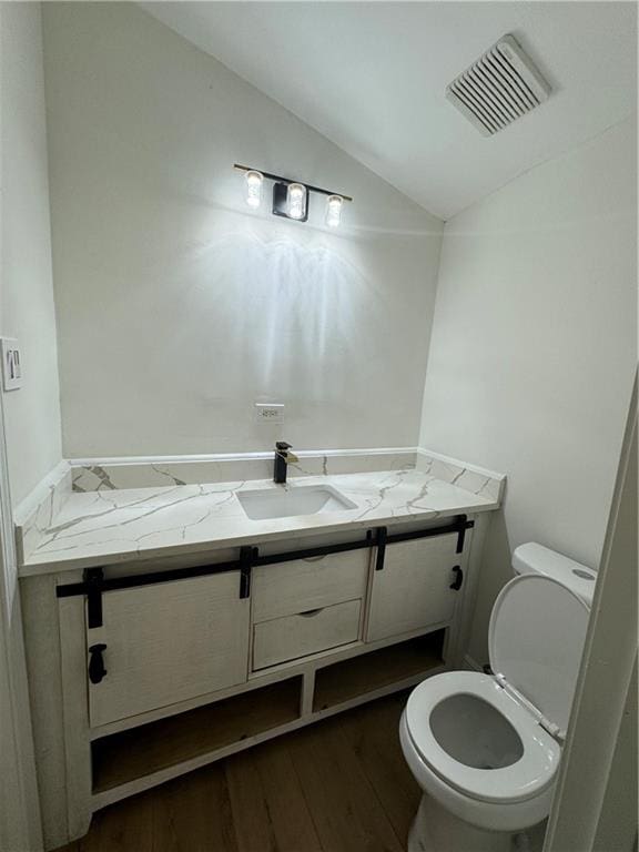 bathroom with hardwood / wood-style floors, lofted ceiling, toilet, and vanity