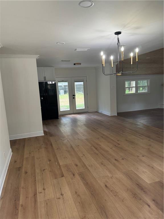 spare room featuring french doors, an inviting chandelier, light hardwood / wood-style flooring, and a healthy amount of sunlight