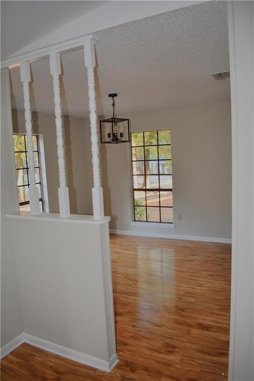 spare room with a textured ceiling, a chandelier, wood finished floors, visible vents, and baseboards