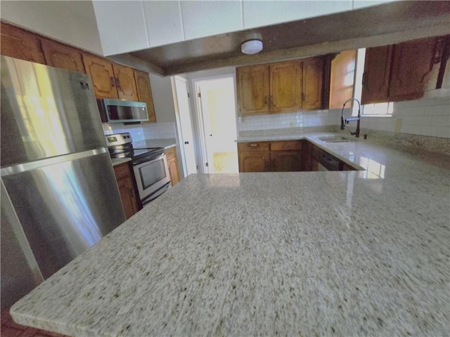 kitchen with stainless steel appliances, brown cabinets, a sink, and decorative backsplash