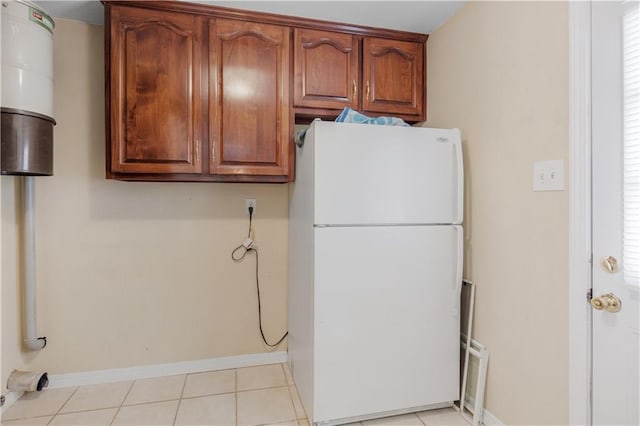 kitchen featuring freestanding refrigerator, brown cabinetry, baseboards, and light tile patterned floors