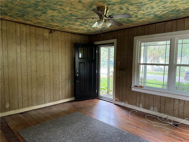 foyer entrance with wood walls, a healthy amount of sunlight, ceiling fan, and dark hardwood / wood-style floors