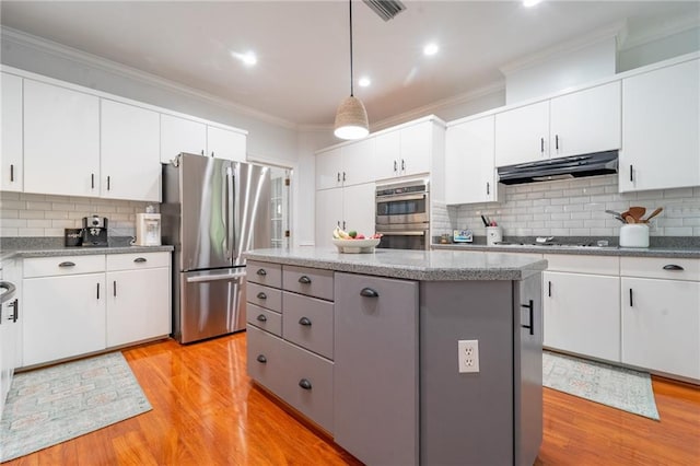 kitchen with ornamental molding, a kitchen island, under cabinet range hood, decorative backsplash, and stainless steel appliances