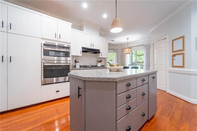 kitchen with a center island, under cabinet range hood, light wood-style floors, and double oven