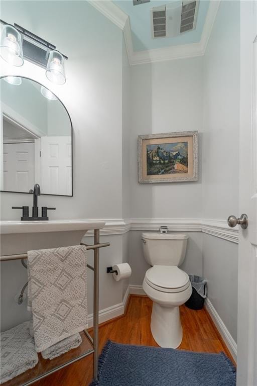 bathroom with baseboards, crown molding, toilet, visible vents, and wood finished floors