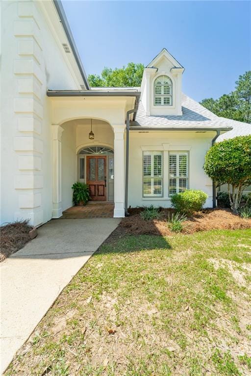 property entrance with stucco siding, french doors, and a lawn