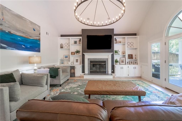 living area featuring built in features, high vaulted ceiling, a glass covered fireplace, a chandelier, and wainscoting