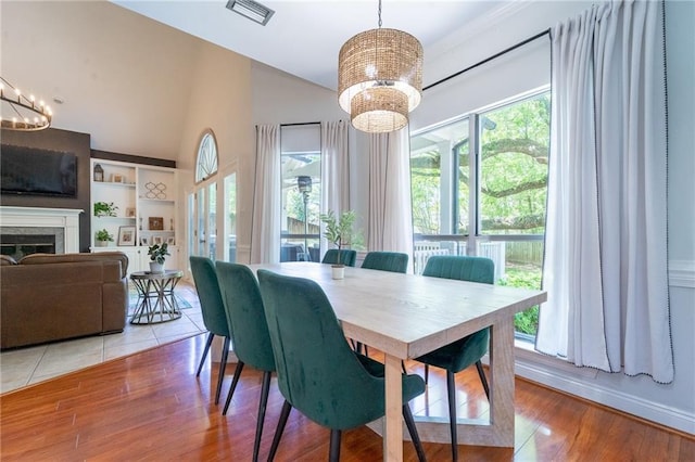 dining space with visible vents, wood finished floors, a chandelier, and a glass covered fireplace
